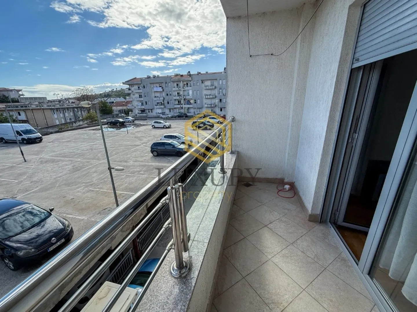 Tiled balcony with metal railing and a view of the parking lot and buildings.