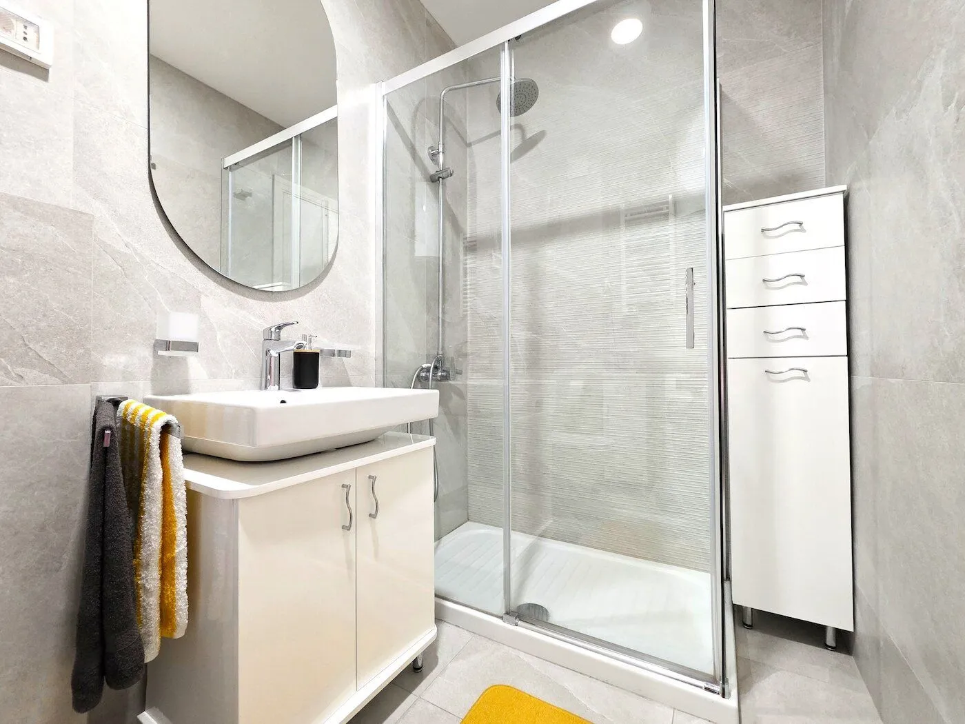 Modern bathroom with a shower cabin, washbasin, and white cabinet.