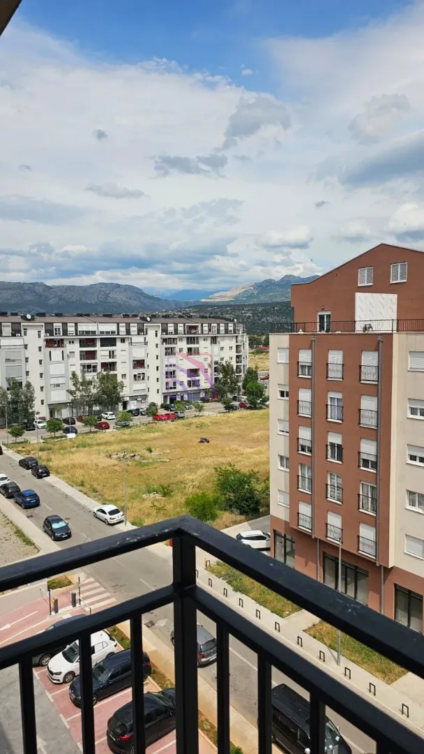 Pogled sa terase na okolne zgrade, parking i planine u daljini.