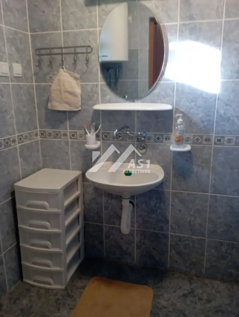 Manje kupatilo sa umivaonikom, ogledalom i pločicama na zidovima.