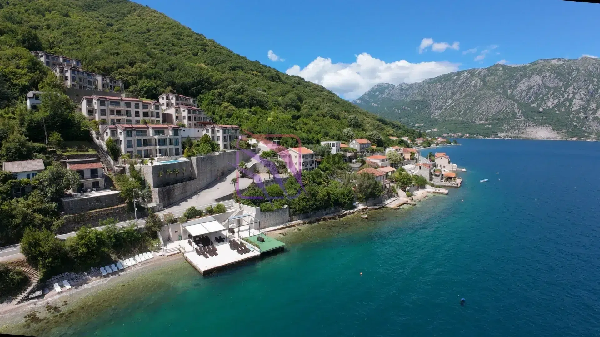 Pogled iz vazduha na kompleks zgrada na obali mora sa plažom.