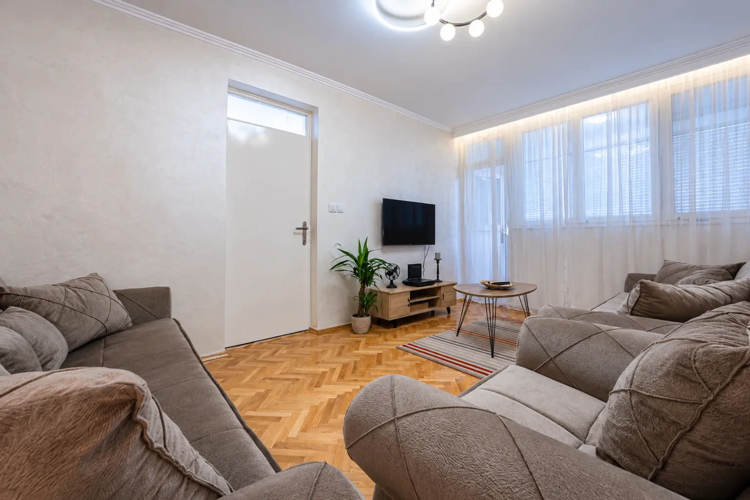 Living room with a sofa set, television, and wooden flooring.