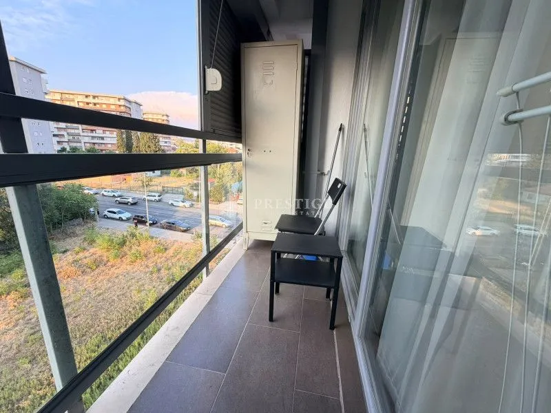 Narrow tiled balcony with a metal cabinet and chairs, overlooking the street.