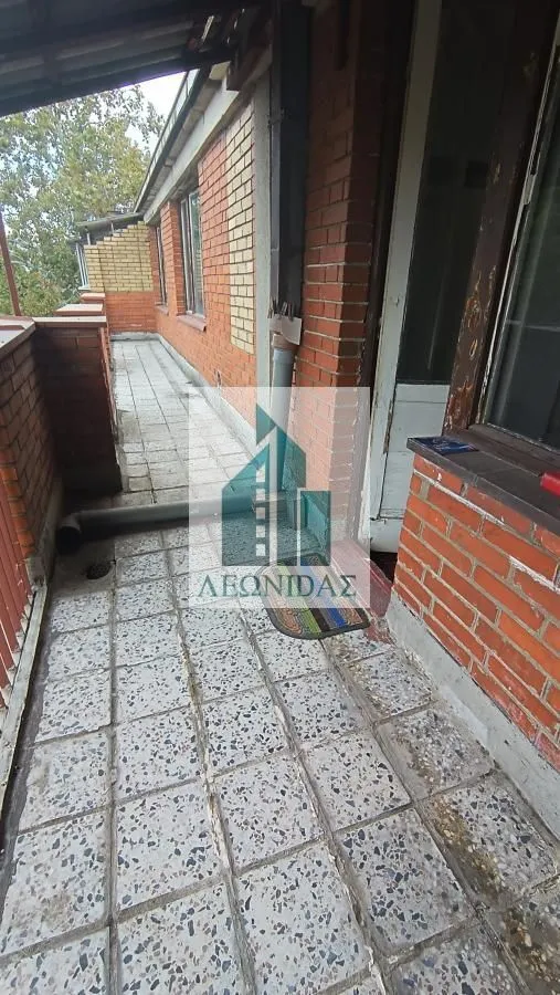 Dugački popločani balkon sa zidom od cigle i ulaznim vratima.