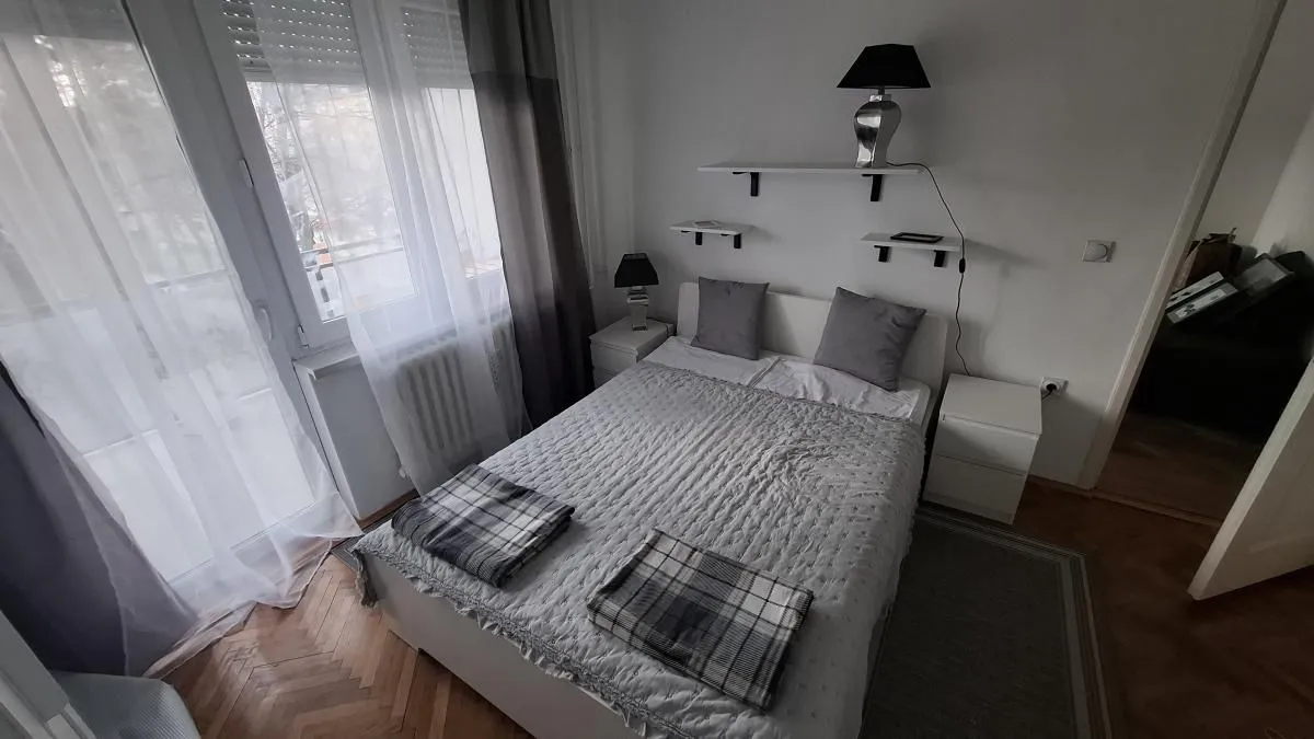 Spavaća soba sa bračnim krevetom, noćnim stočićima i izlazom na balkon.