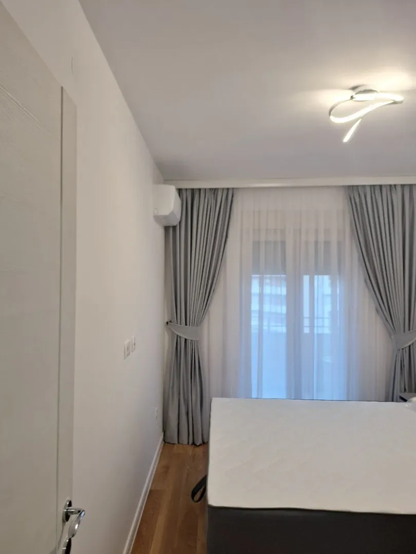 Svijetla spavaća soba sa modernim osvjetljenjem i sivim zavjesama.