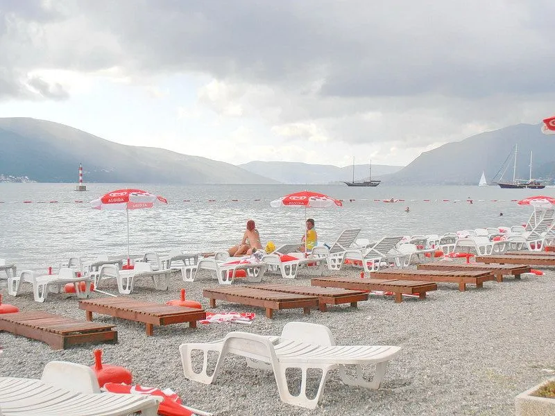 Pogled na šljunkovitu plažu sa ležaljkama i morem u pozadini.