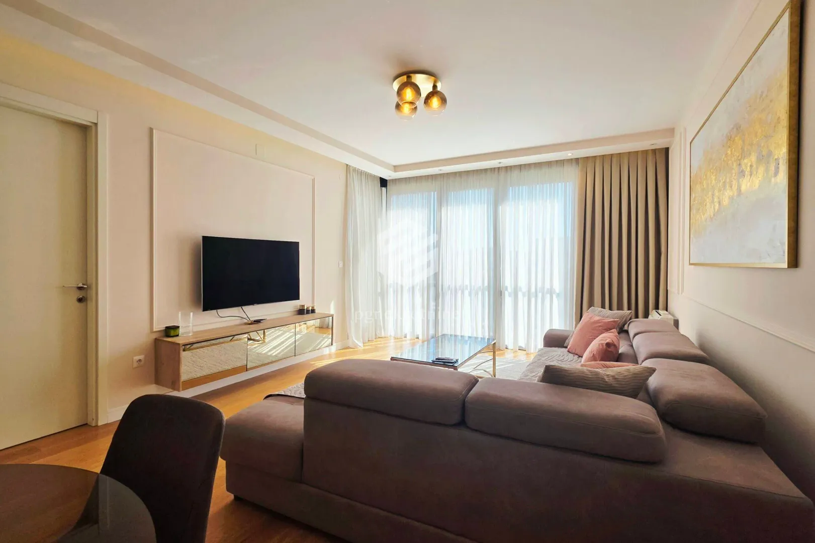 Living room with a sectional sofa, TV, and large windows.