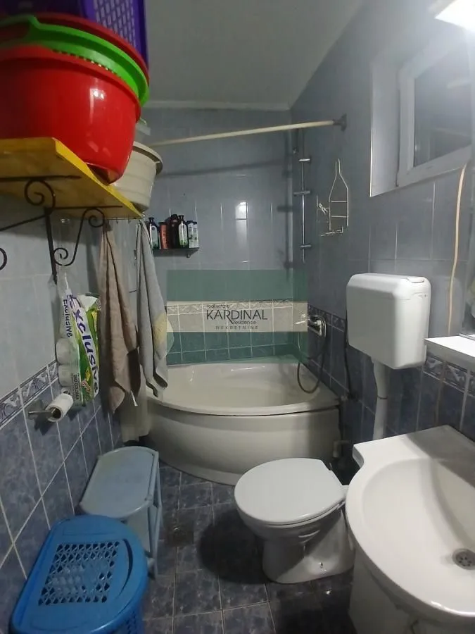 Manje kupatilo sa kadom, toaletom i umivaonikom obloženo pločicama.