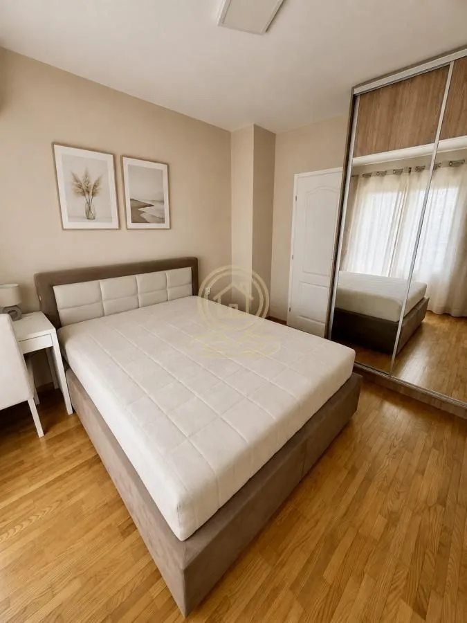 Furnished bedroom with a double bed, mirrored wardrobe, and hardwood flooring.