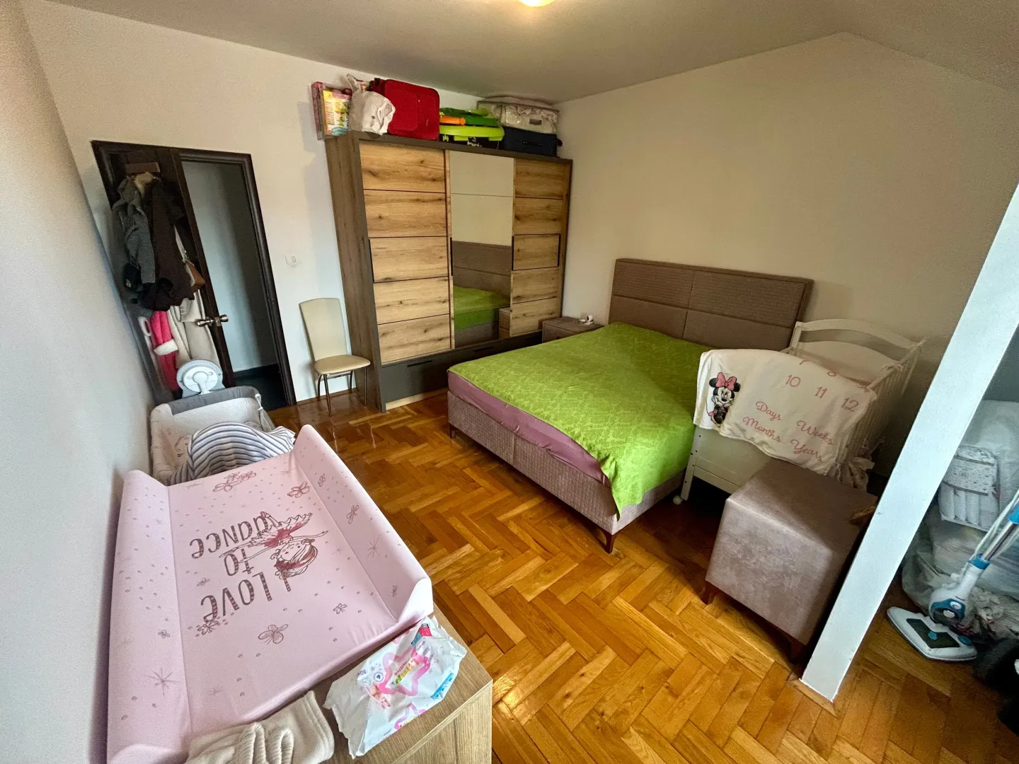 Spavaća soba sa krevetom, ormarom i dječijim krevetcem.