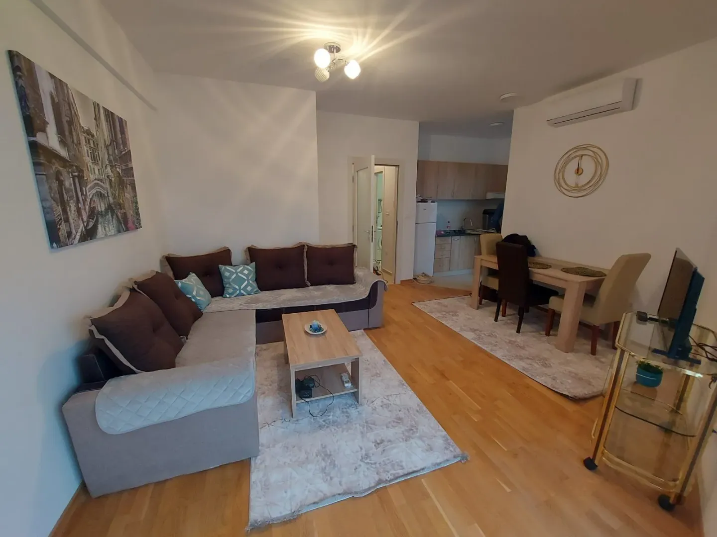 Bright living room with a corner sofa, dining area, and kitchen in the background.