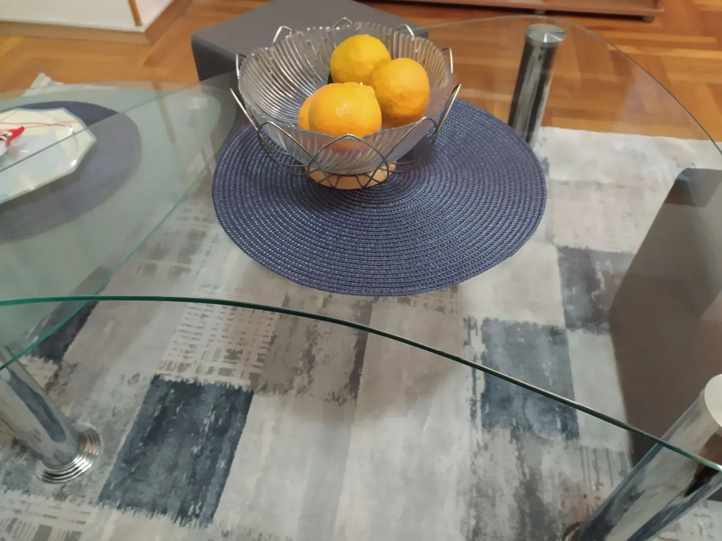 Glass coffee table with a bowl of oranges on a rug in a living room.