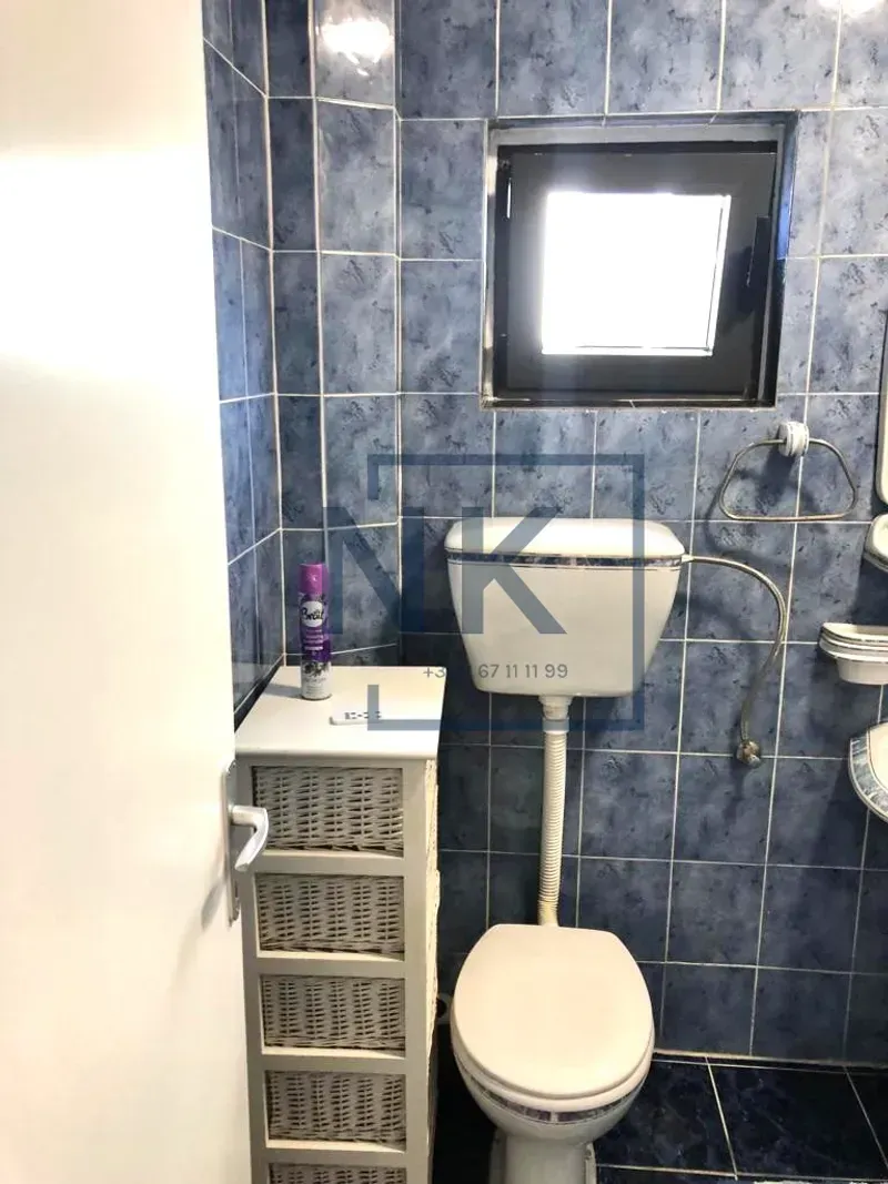 Small bathroom tiled in blue with a toilet and a window.