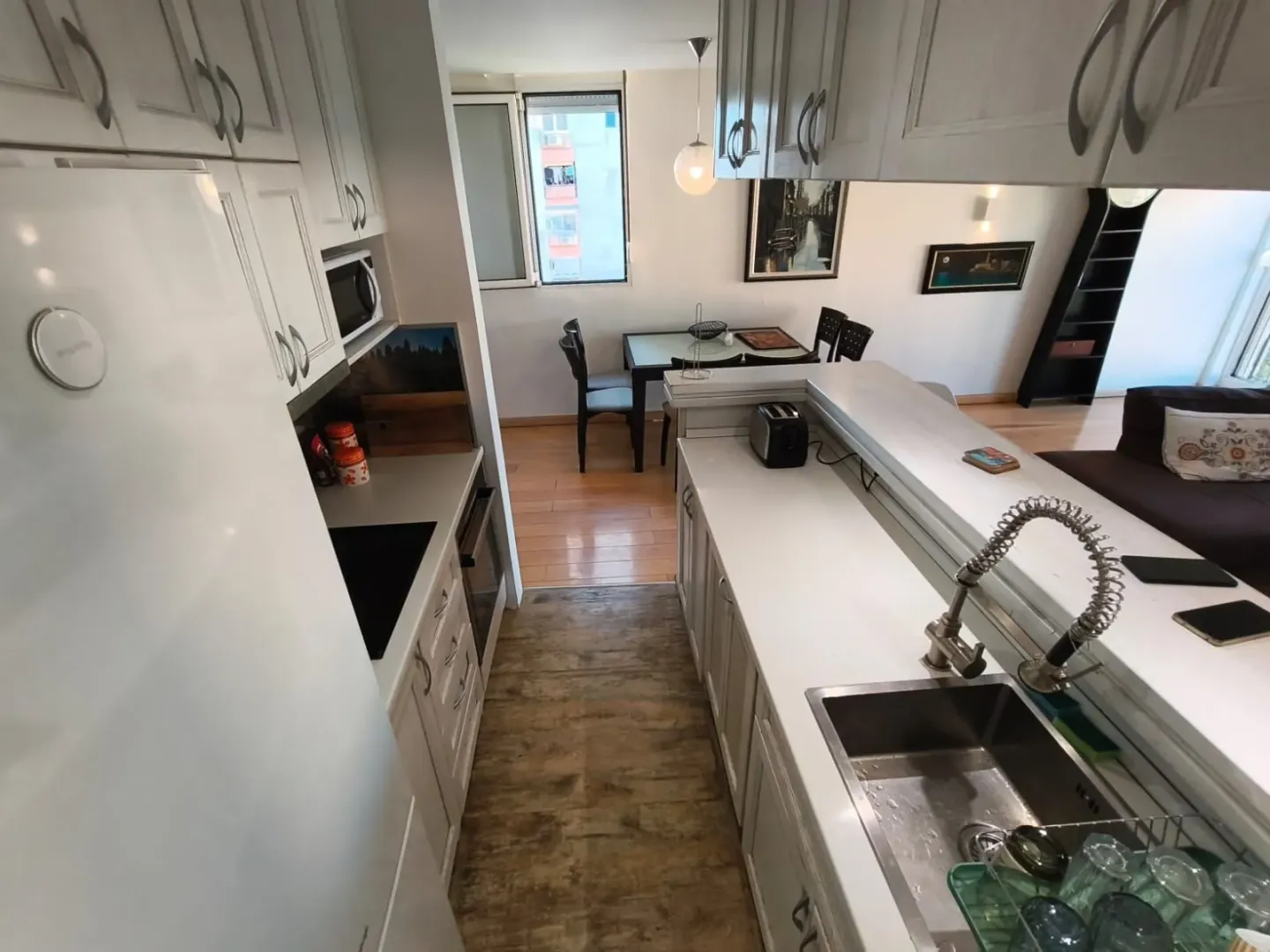 Compact kitchen with white cabinetry and a dining area in the background.