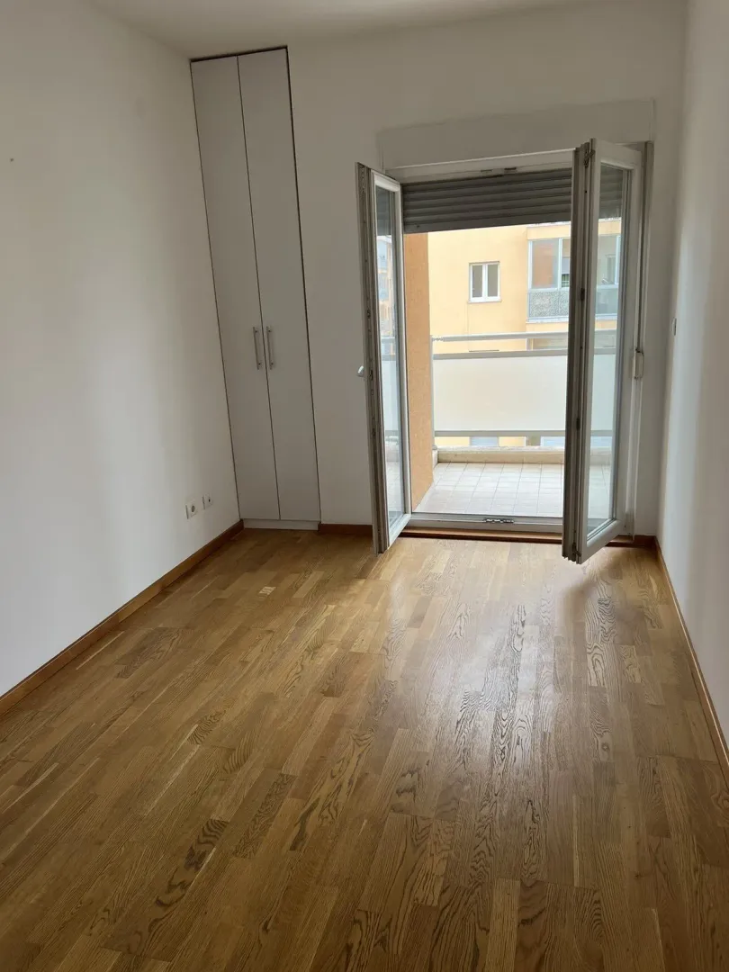 Bright empty room with parquet flooring, a built-in wardrobe, and balcony access.