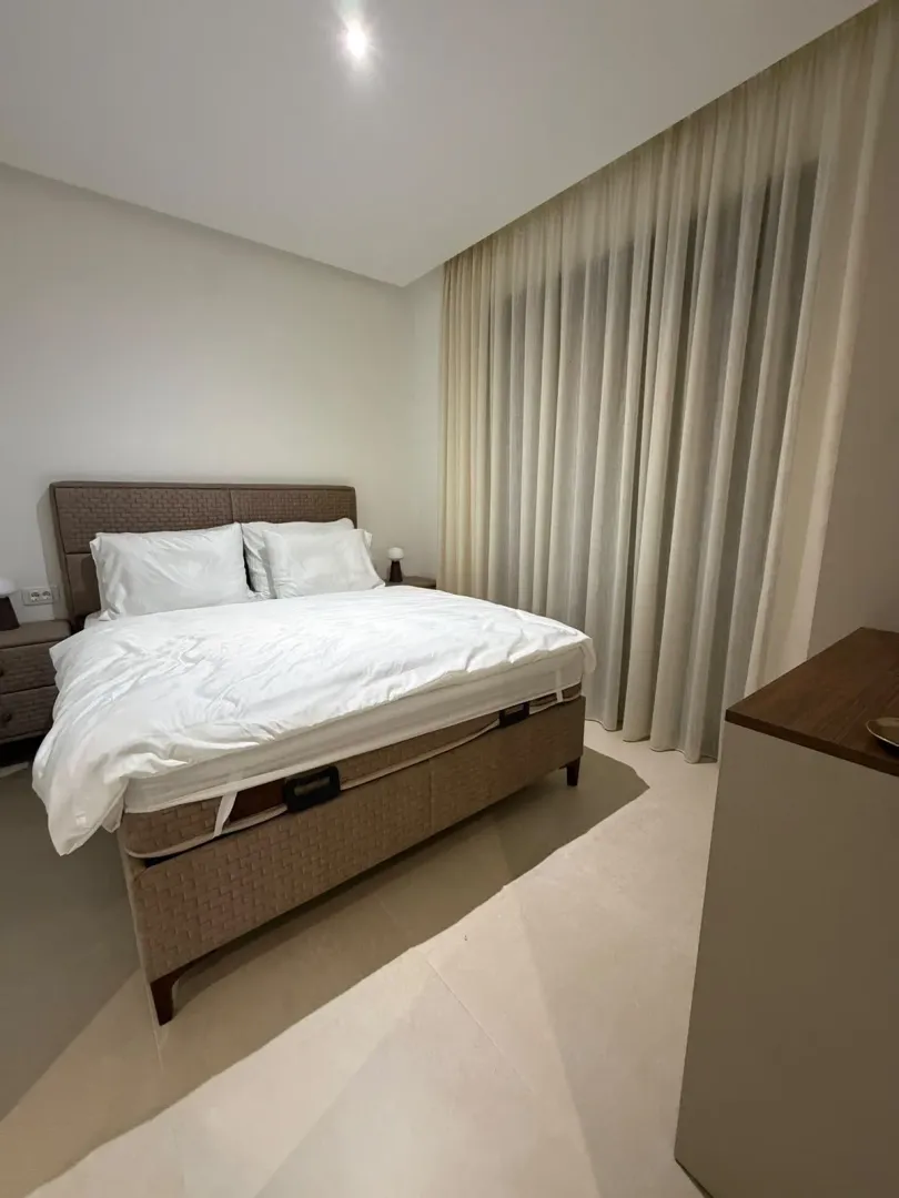 Modern bedroom with a double bed and light curtains.