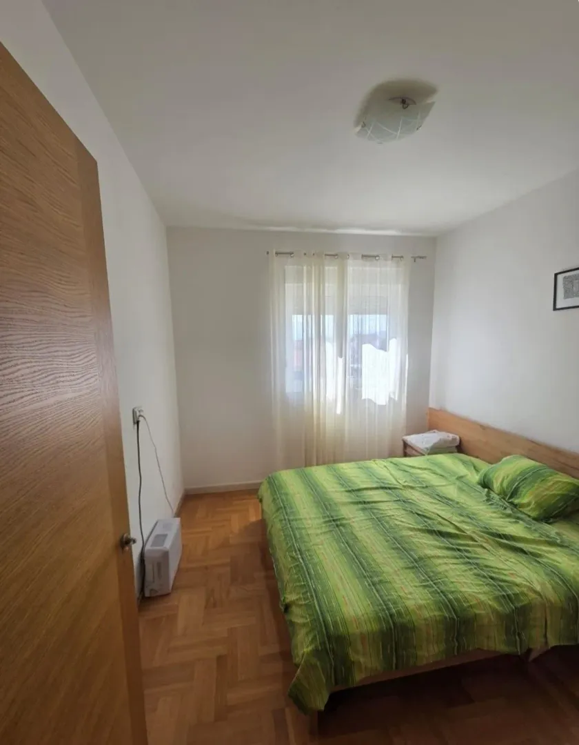 Namještena spavaća soba sa bračnim krevetom, parketom i prozorom.