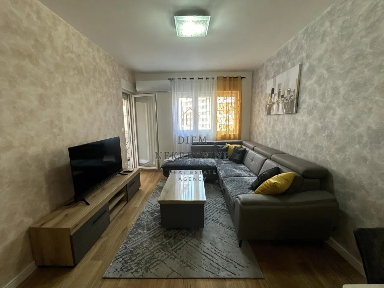 Dnevna soba sa garniturom, televizorom i izlazom na terasu.