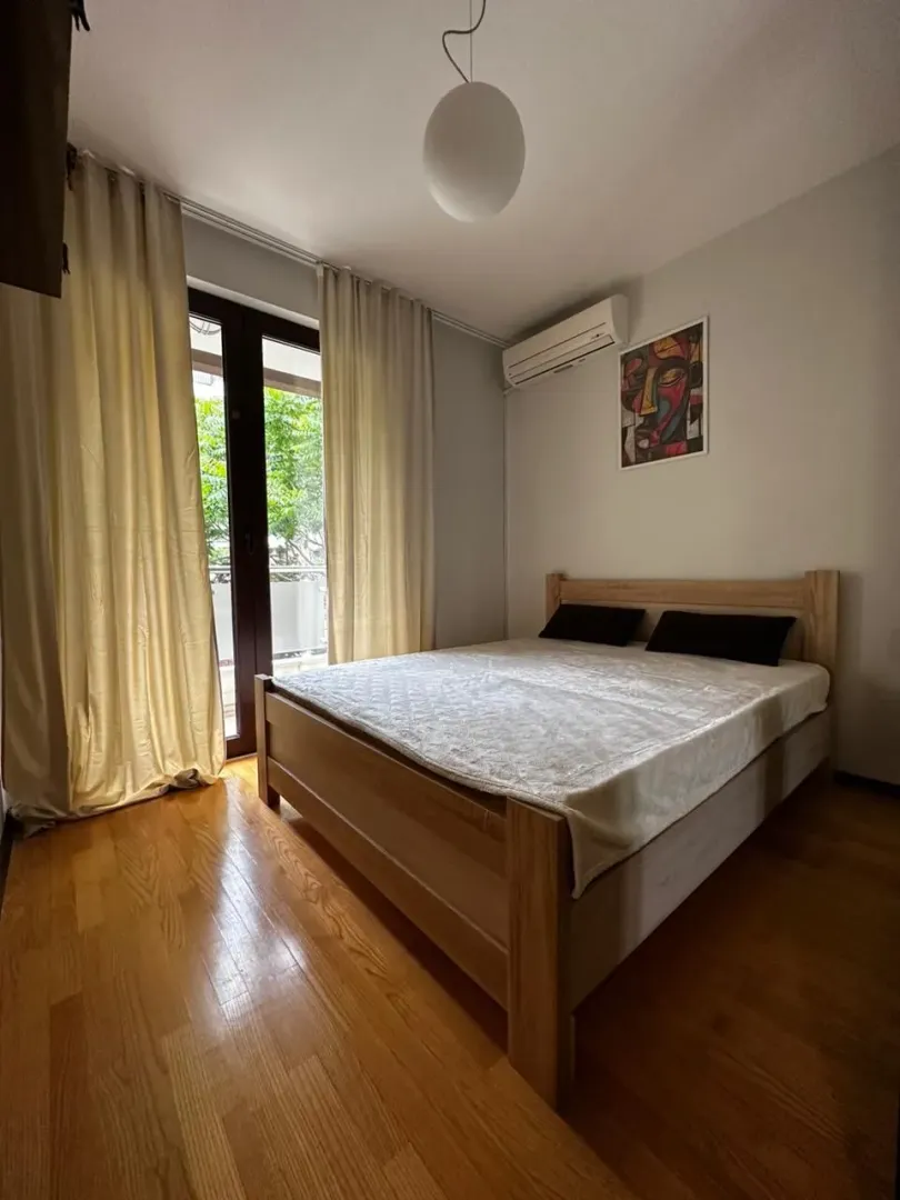 Namještena spavaća soba sa bračnim krevetom, drvenim podom i izlazom na balkon.