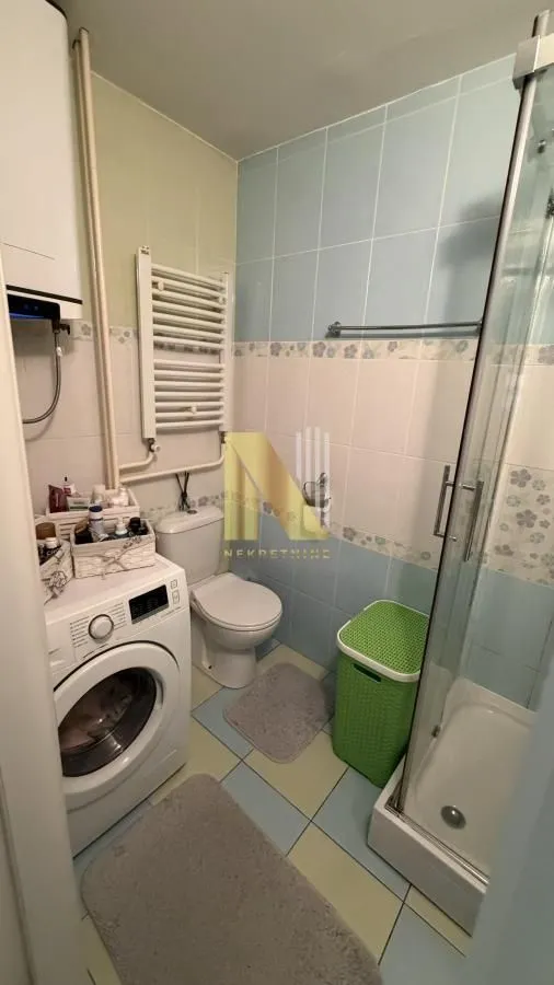 Manje kupatilo sa tuš kabinom, veš mašinom i sanitarijama.