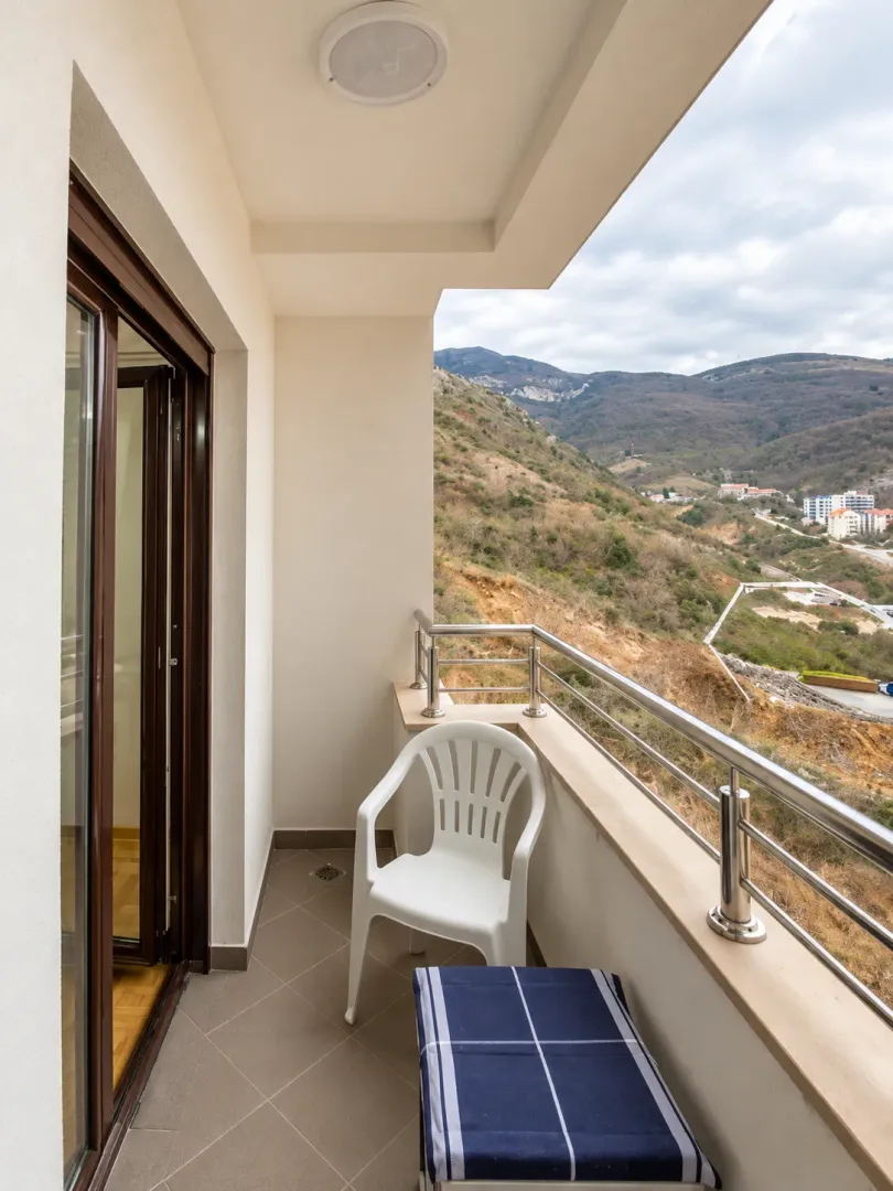 Natkriveni balkon sa staklenom ogradom i pogledom na okolna brda.