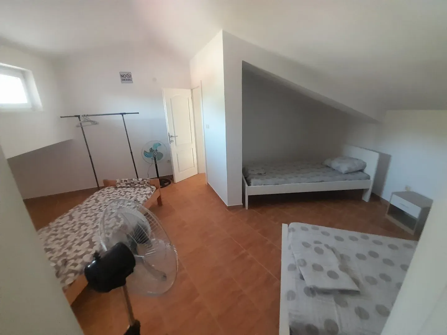 Attic room furnished with multiple beds and fans.