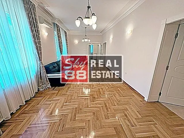Spacious living room with herringbone parquet flooring and large windows.