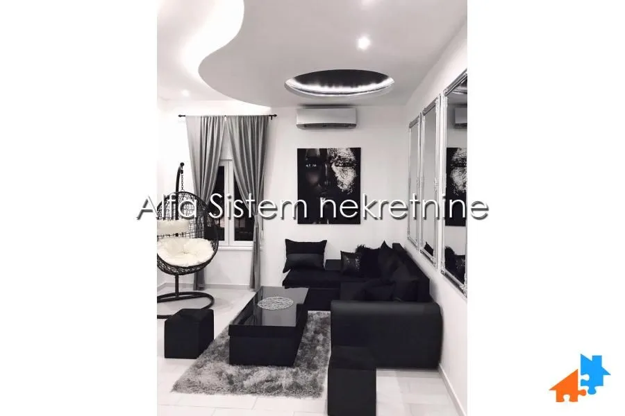Dnevna soba sa crnim garniturama, visećom foteljom i modernim plafonom.