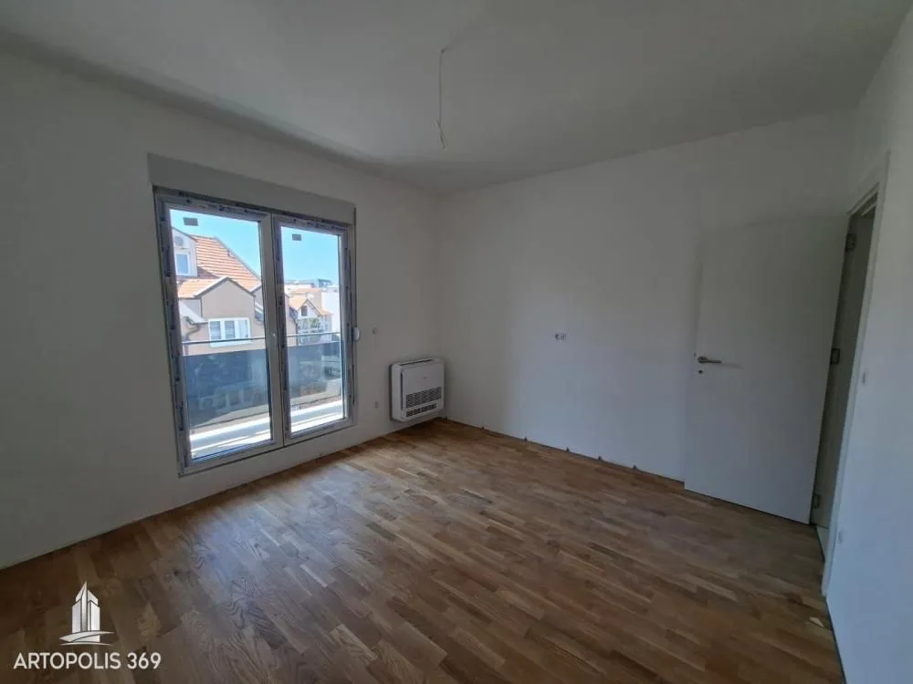 Prazna soba sa parketom i balkonskim vratima.