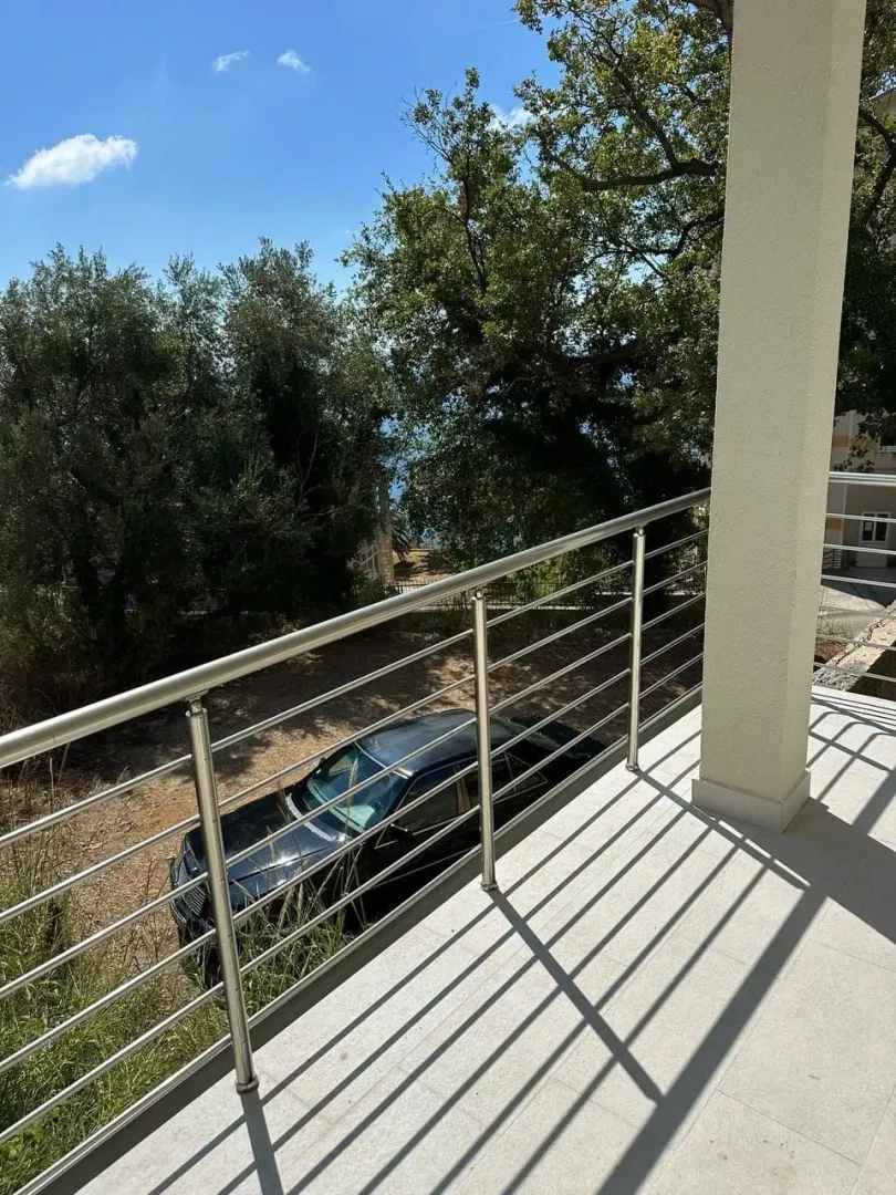 Prostrana terasa sa metalnom ogradom i pogledom na dvorište i zelenilo.