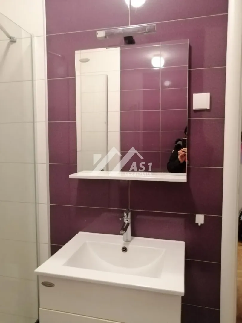 Kupatilo sa umivaonikom, ogledalom i ljubičastim pločicama.