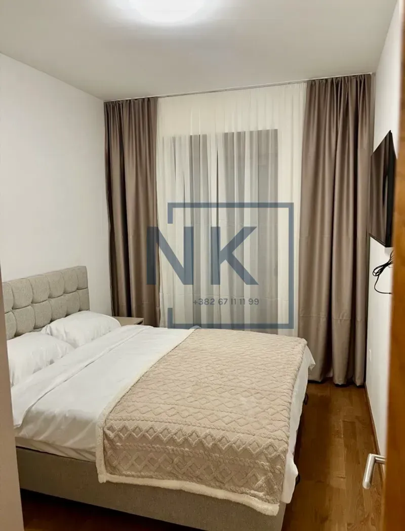 Furnished bedroom with a double bed and a window with curtains.