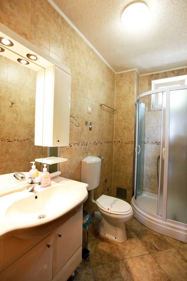 Compact bathroom with a shower cabin, washbasin, and toilet in beige tiles.
