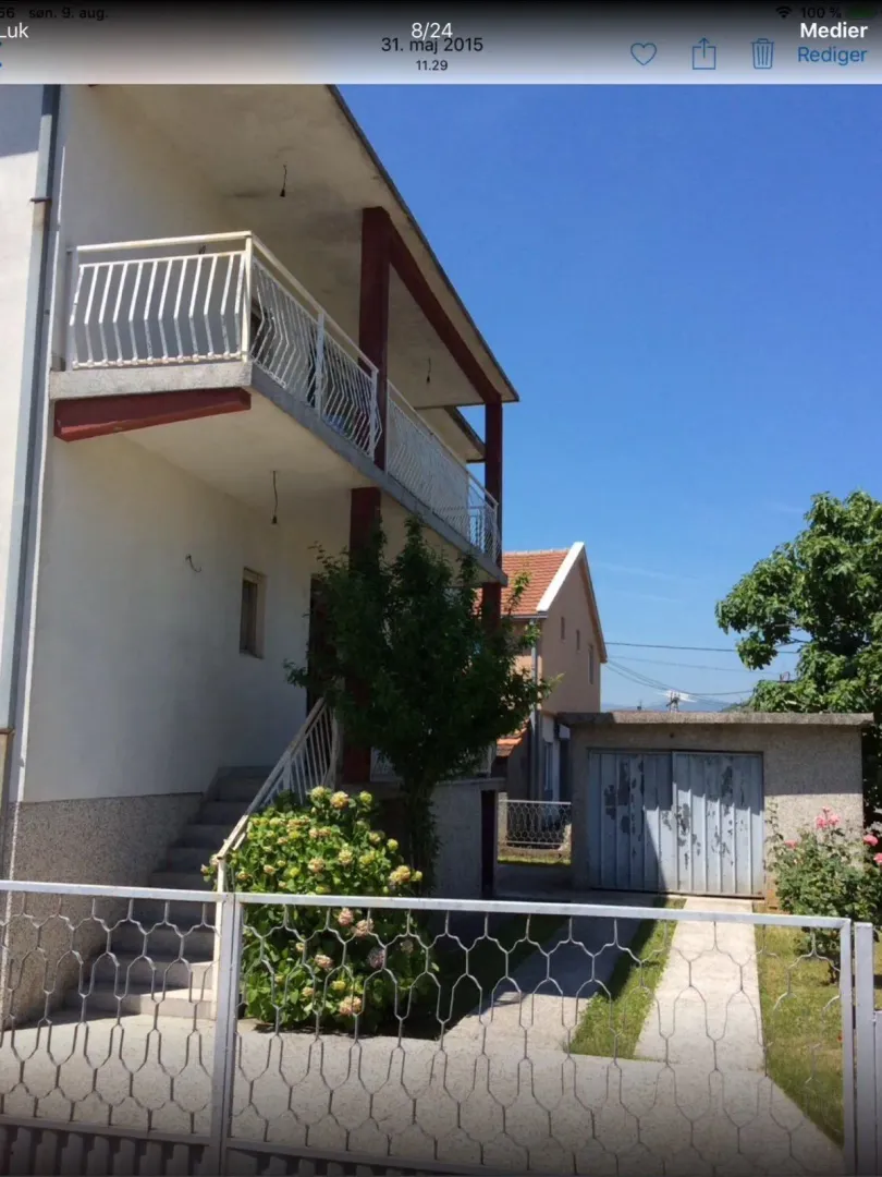Vanjski izgled dvospratne kuće sa ograđenim dvorištem i garažom.
