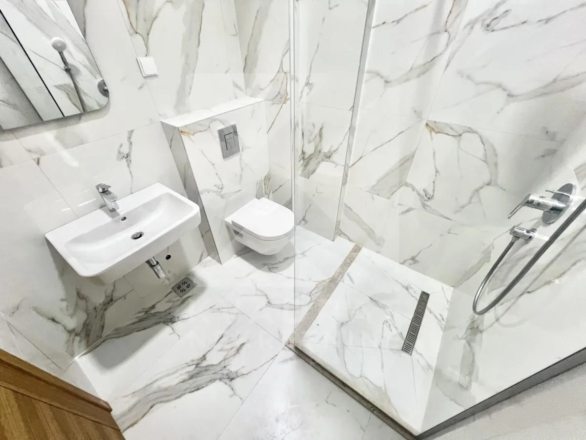 Modern bathroom equipped with marble tiles, washbasin and a walk-in shower.