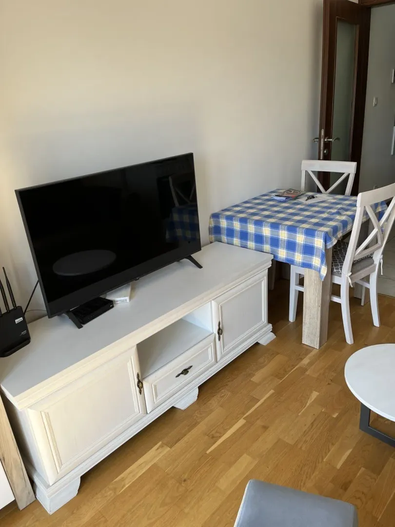 Part of a living room featuring a TV on a white stand and a dining table.