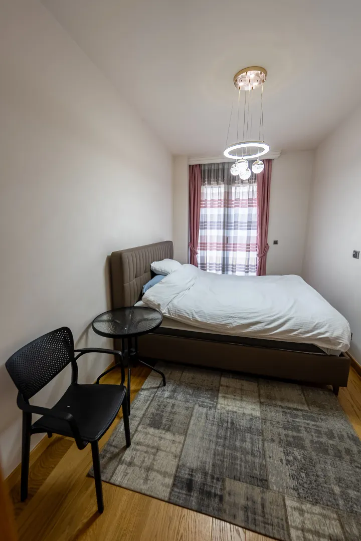 Bedroom with a double bed, small table, chair, and modern chandelier.
