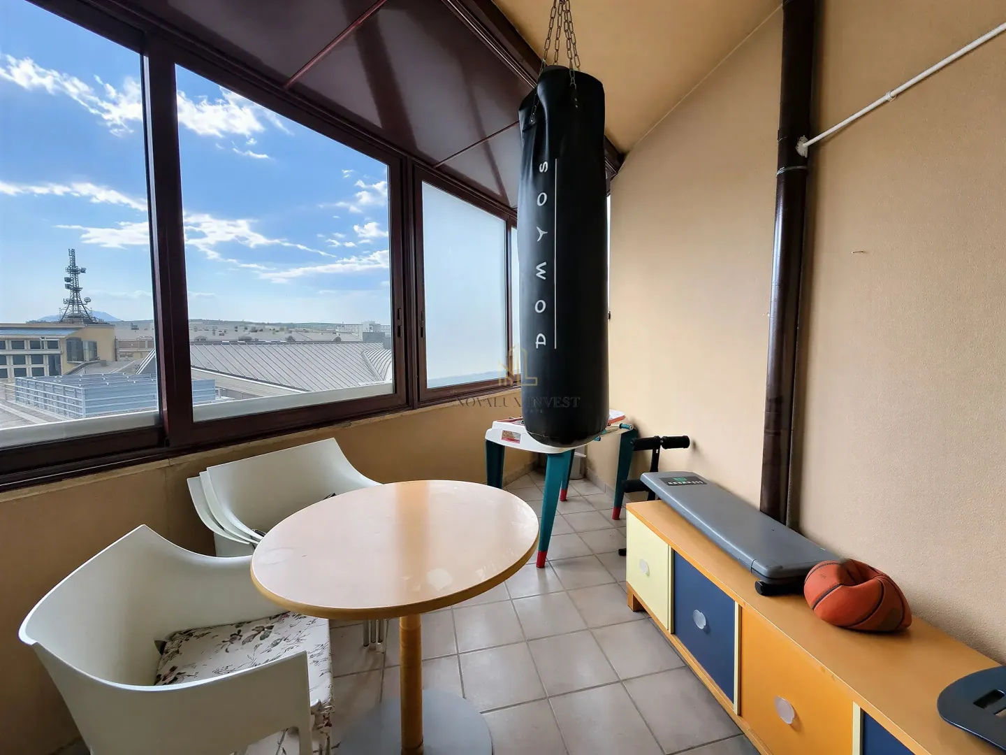Enclosed balcony with seating furniture and sports equipment.