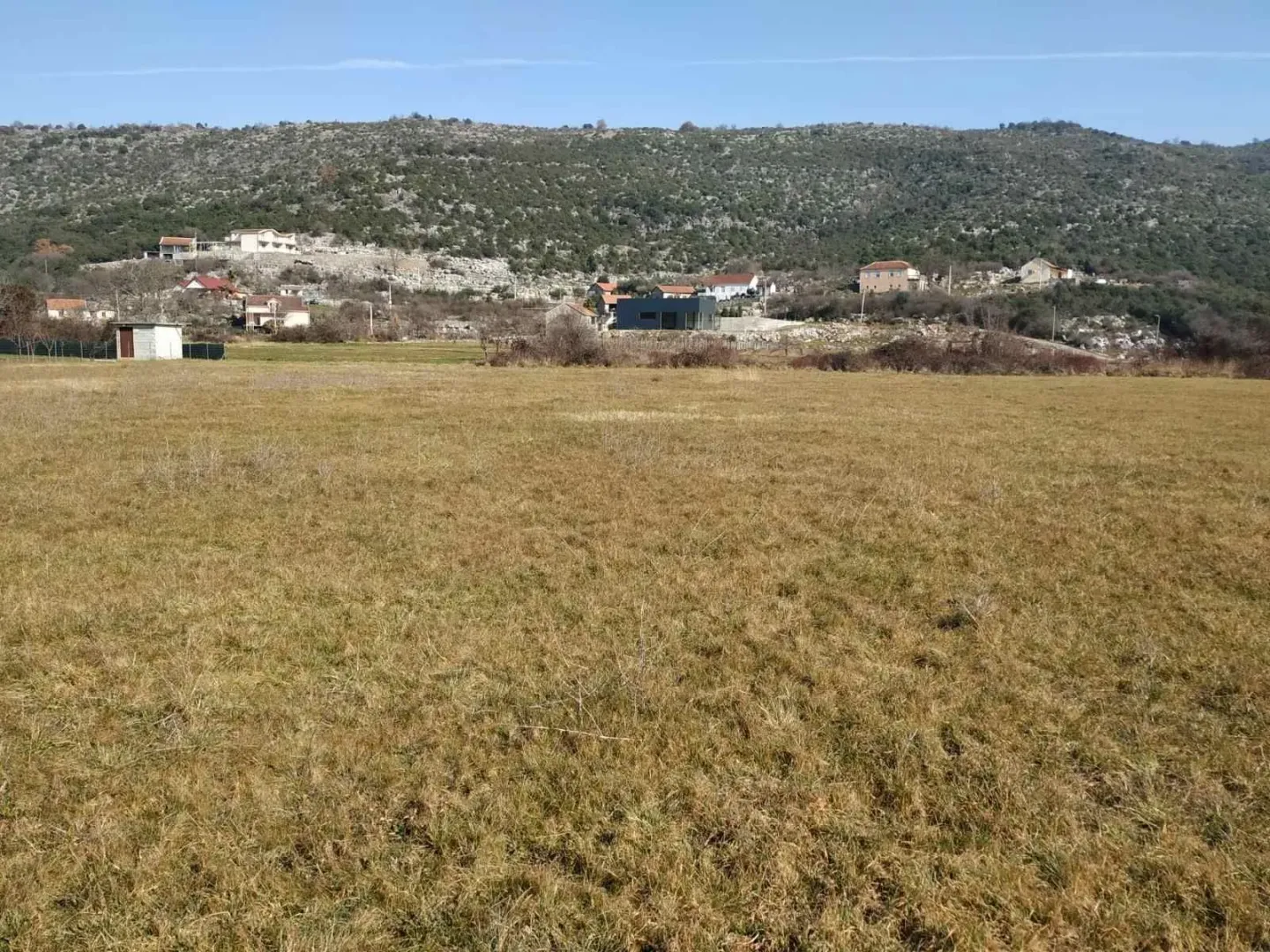 Pogled na prostrano zemljište sa okolnim brdima i kućama u pozadini.