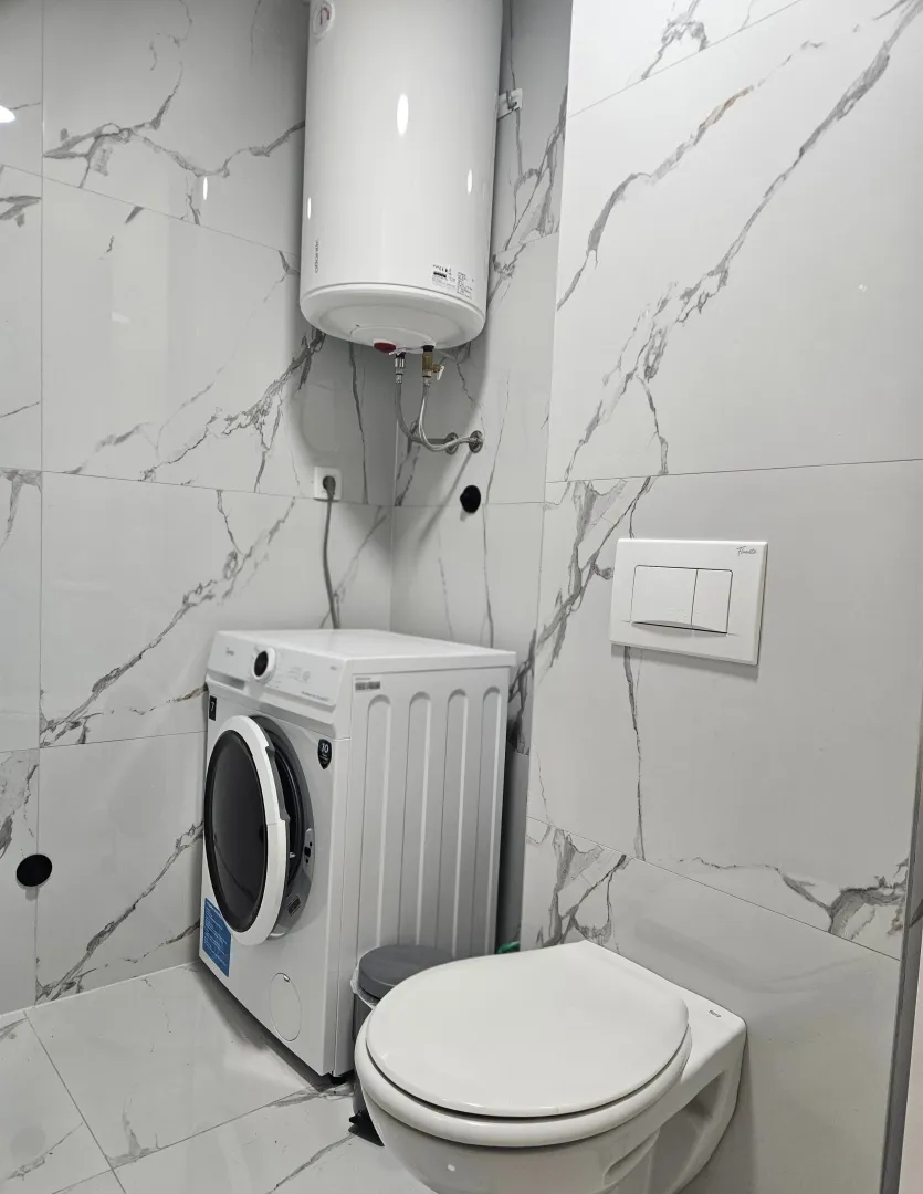 Modernly equipped bathroom with a washing machine and white marble tiles.
