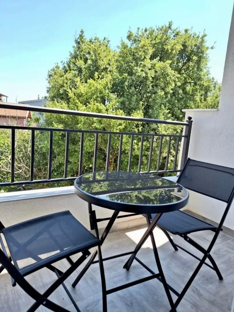 Small balcony with a black glass table and two chairs, overlooking greenery.