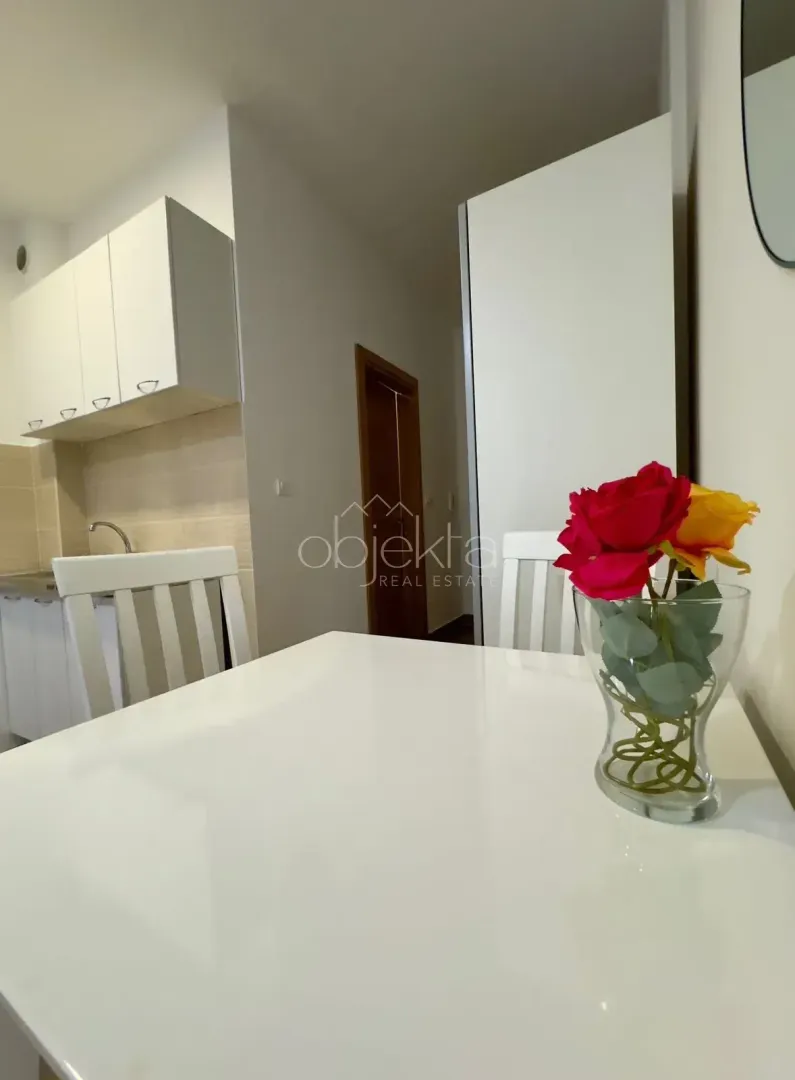 Dining table with a vase of flowers and the kitchen in the background.