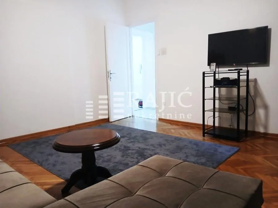 Living room with seating furniture, coffee table, television, and hardwood flooring.