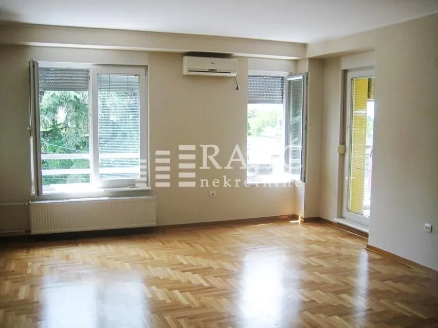 Empty living room with parquet flooring, white walls, and two windows.