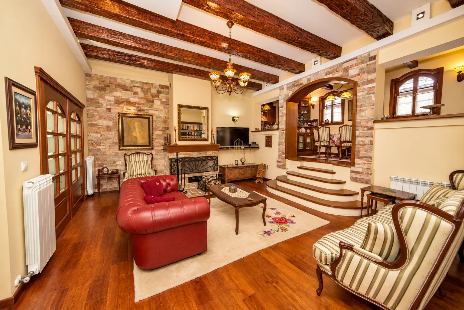 Prostrana dnevna soba sa kaminom, drvenim gredama na plafonu i stilskim namještajem.