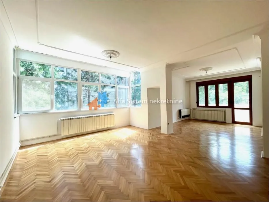 Empty living room with large windows and parquet flooring.