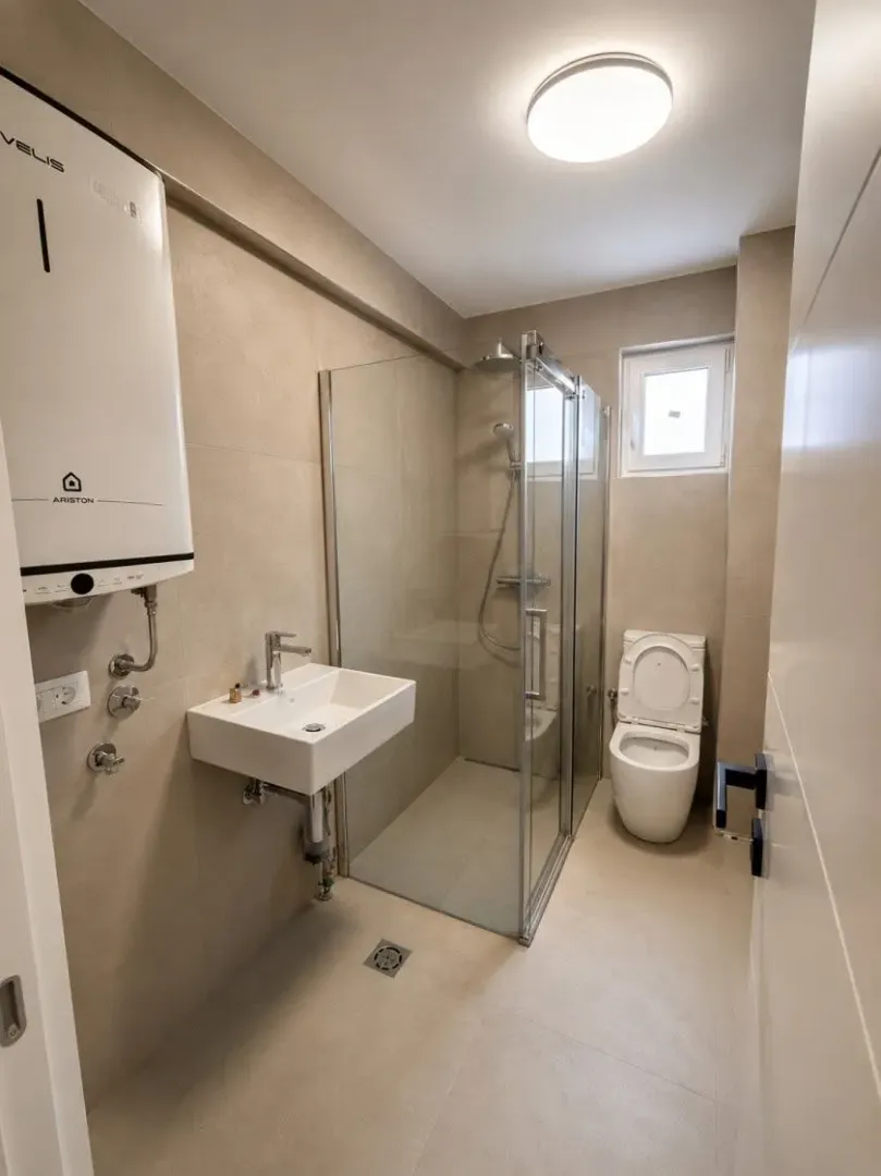 Moderne kupatilo sa tuš kabinom, umivaonikom i wc šoljom u bež tonovima.