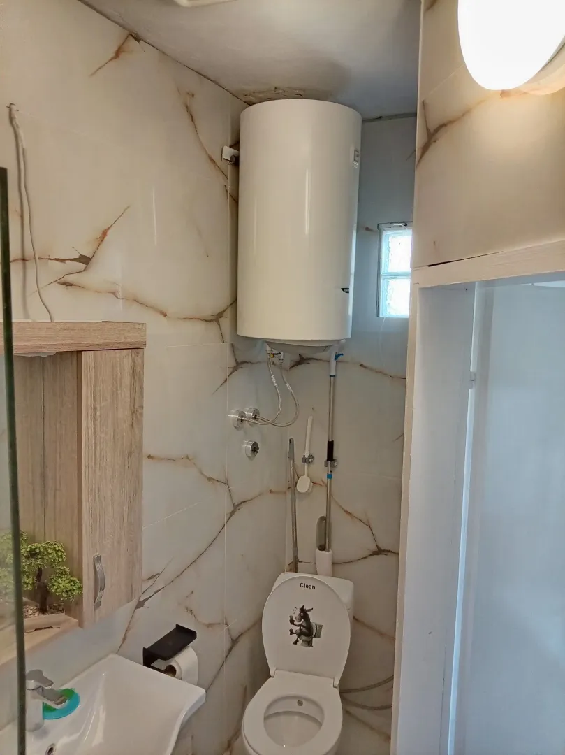 Manje kupatilo sa wc šoljom, umivaonikom i bojlerom na zidu.