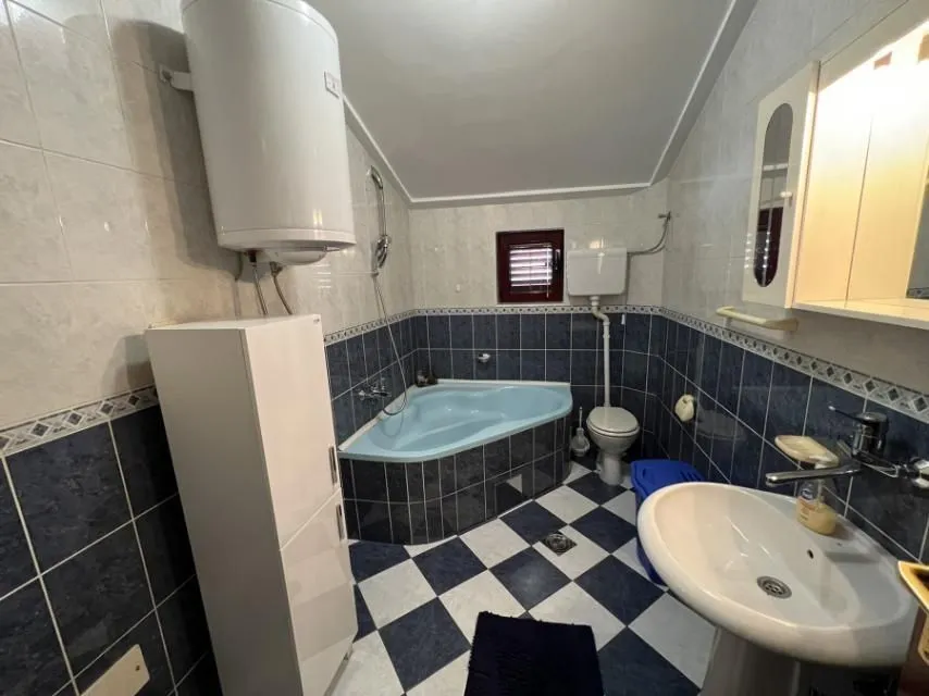 Bathroom with blue and white tiles, a corner bathtub, and a boiler.